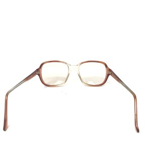 May include: A pair of eyeglasses with a light brown frame and clear lenses. The rectangular frames transition to a silver and brown arm. The glasses are set against a white background.
