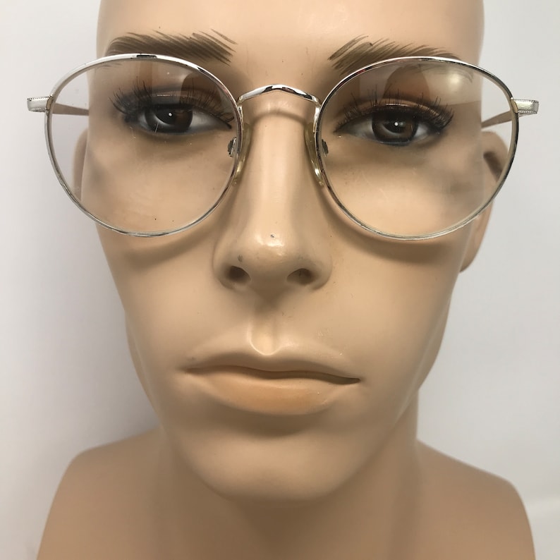 Peut inclure: Lunettes &agrave; monture argent&eacute;e avec des verres ronds. Les lunettes ont une monture m&eacute;tallique fine et sont pr&eacute;sent&eacute;es sur un mannequin. Les verres sont clairs et le design est classique et minimaliste.
