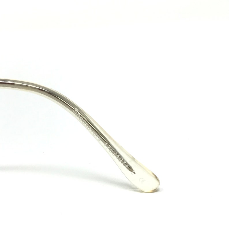 May include: Close-up of a silver-toned eyeglass frame arm. The arm has the text "Specsavers 1753197+" printed on it. The frame is made of a shiny, metallic material.