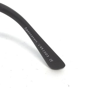 Pu&ograve; includere: Primo piano di un'asta di occhiali nera con la scritta "Specsavers 1451003 CE" stampata in bianco. L'asta &egrave; angolata e lo sfondo &egrave; bianco.