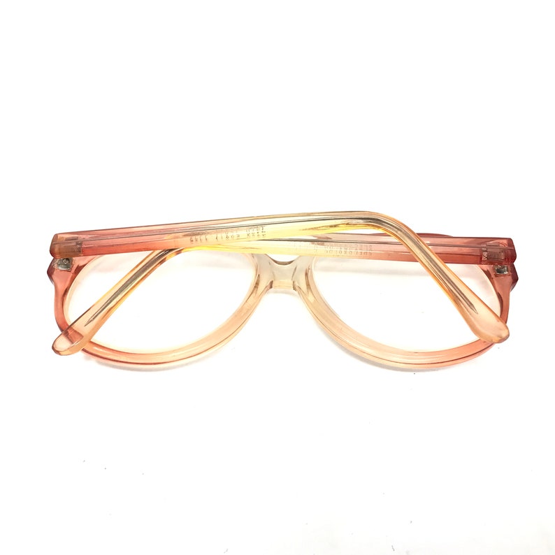 May include: A pair of vintage eyeglasses with a light brown and peach gradient frame. The frame is made of plastic and has a rounded shape.