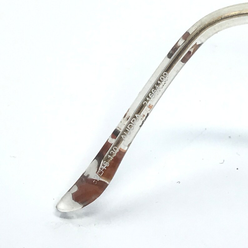 May include: Close-up of the arm of a pair of eyeglasses with the text "D46 130 AUDPA 2166 4100" printed on the inside of the arm.