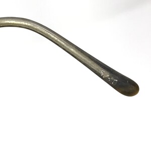 Puede incluir: Primer plano de una patilla de gafas de metal plateado con el n&uacute;mero "51-16" grabado en el lateral.