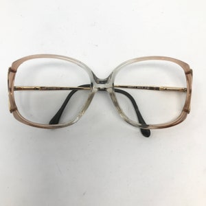 May include: Oversized eyeglasses with a gradient frame, transitioning from a light brown to a clear hue. The frames have gold-colored metal accents and black temples. The text on the frame reads "SPEC SAVERS" and "AB6051 2 54/15 A160".