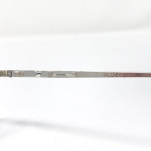 Peut inclure: Gros plan sur une branche de monture de lunettes en m&eacute;tal argent&eacute;. Le texte "ERS FP 1342 107" est imprim&eacute; sur la branche. La monture est fine et semble &ecirc;tre en m&eacute;tal l&eacute;ger.