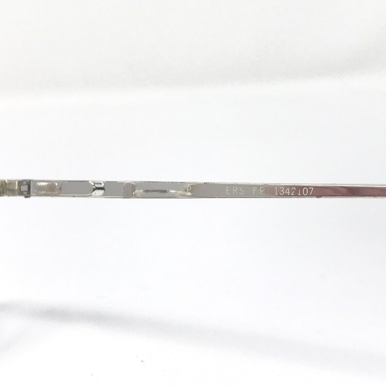 Peut inclure: Gros plan sur une branche de monture de lunettes en m&eacute;tal argent&eacute;. Le texte "ERS FP 1342 107" est imprim&eacute; sur la branche. La monture est fine et semble &ecirc;tre en m&eacute;tal l&eacute;ger.