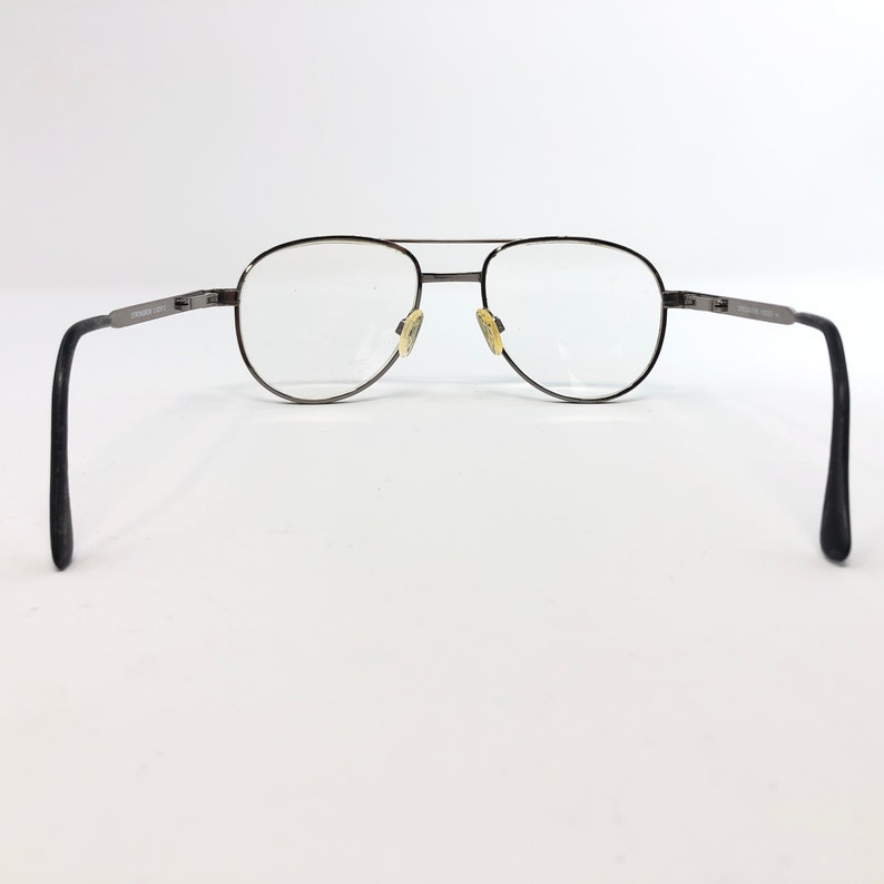 Peut inclure: Une paire de lunettes de vue aviateur vintage avec une monture en m&eacute;tal fonc&eacute;. Les verres sont clairs et les plaquettes nasales sont jaunies. Les branches sont sombres et comportent du texte. Fond blanc.