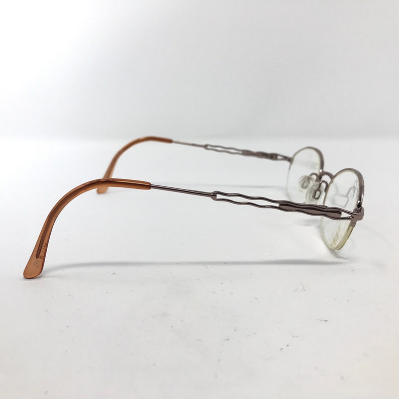 K&ouml;nnte beinhalten: Eine silberfarbene Brille mit braunen B&uuml;gelenden. Die Brille hat ein randloses Design und eine gewellte Br&uuml;cke.