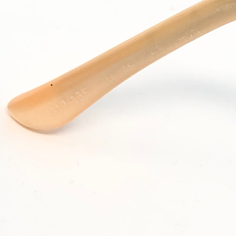 May include: Close-up of a light beige eyeglass arm. The arm has the text "117-135" printed on it. The arm is angled and appears to be made of plastic.