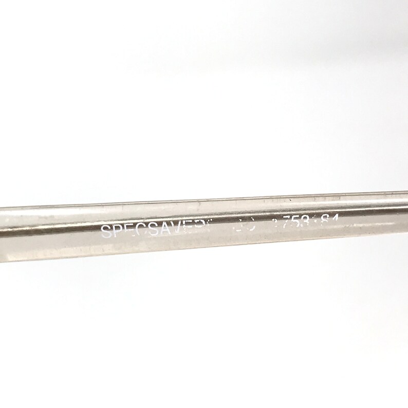 May include: Close-up of a clear eyeglass frame arm with the text "SPECSAVERS" and the numbers "758 84" printed in white. The frame arm is made of a transparent material.