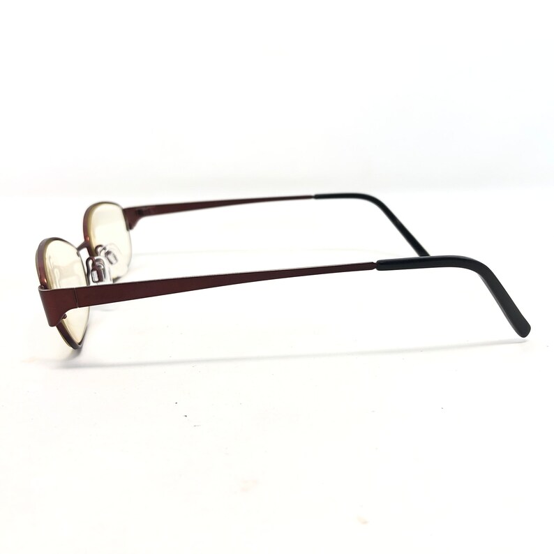 May include: A pair of eyeglasses with a dark brown frame and oval lenses. The temples are a dark brown color that transitions to black at the ear pieces. The glasses are set against a white background.