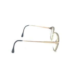 May include: A pair of eyeglasses with a gold-colored metal frame and clear lenses. The temples are thin and extend to curved, dark-colored earpieces. The glasses are set against a white background.