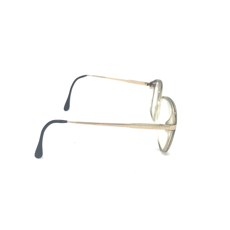 May include: A pair of eyeglasses with a gold-colored metal frame and clear lenses. The temples are thin and extend to curved, dark-colored earpieces. The glasses are set against a white background.