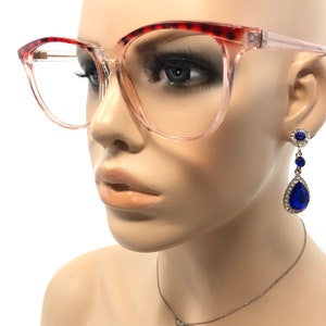 May include: Clear-framed eyeglasses with a red tortoiseshell pattern on the top rims. A mannequin wears the glasses and a pair of dangling earrings with blue teardrop-shaped gems and silver accents. A silver necklace is also visible.