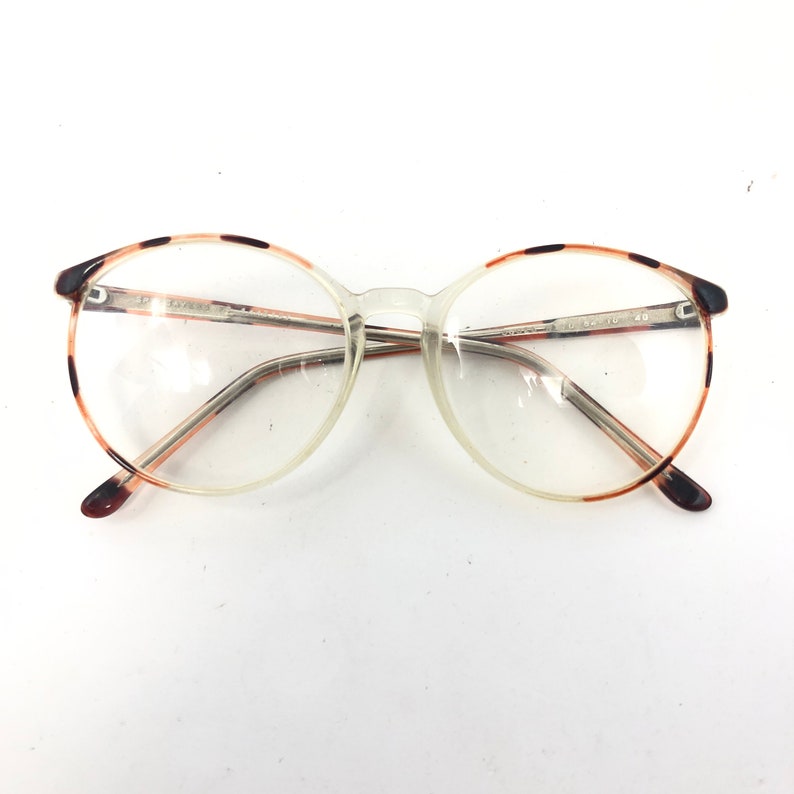 K&ouml;nnte beinhalten: Klare Brille mit rundem Rahmen und Schildpattmuster an den oberen R&auml;ndern und B&uuml;geln. Die Gl&auml;ser sind klar, und der Rahmen besteht aus einer Mischung aus klarem Kunststoff und Metall. Die Brille hat einen klassischen, Vintage-Look.