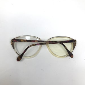 May include: Clear-framed eyeglasses with a patterned design on the temples and bridge. The frames have an oval shape. The temples feature a pattern of brown, yellow, and pink. The lenses are clear.