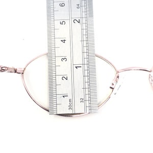 K&ouml;nnte beinhalten: Ros&eacute;goldene ovale Brille mit klaren Gl&auml;sern wird mit einem Lineal gemessen. Das Lineal zeigt, dass die Brille etwa 5 cm breit ist. Die Brille hat einen d&uuml;nnen Rahmen und ein klassisches Design.