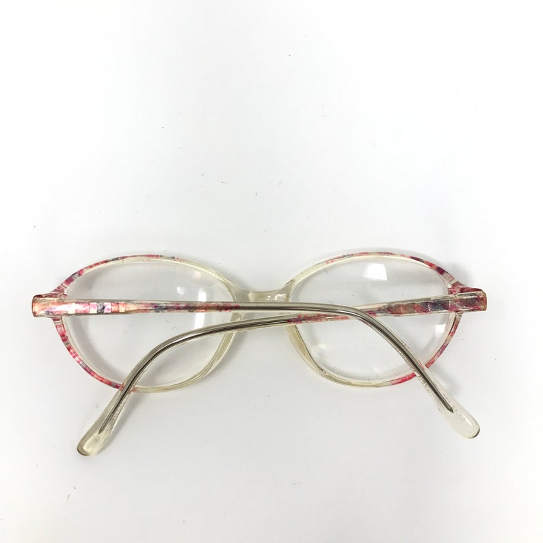 May include: Clear oval eyeglasses with a floral pattern on the frames. The frames have a pink, red, and white design. The arms are silver-toned metal.