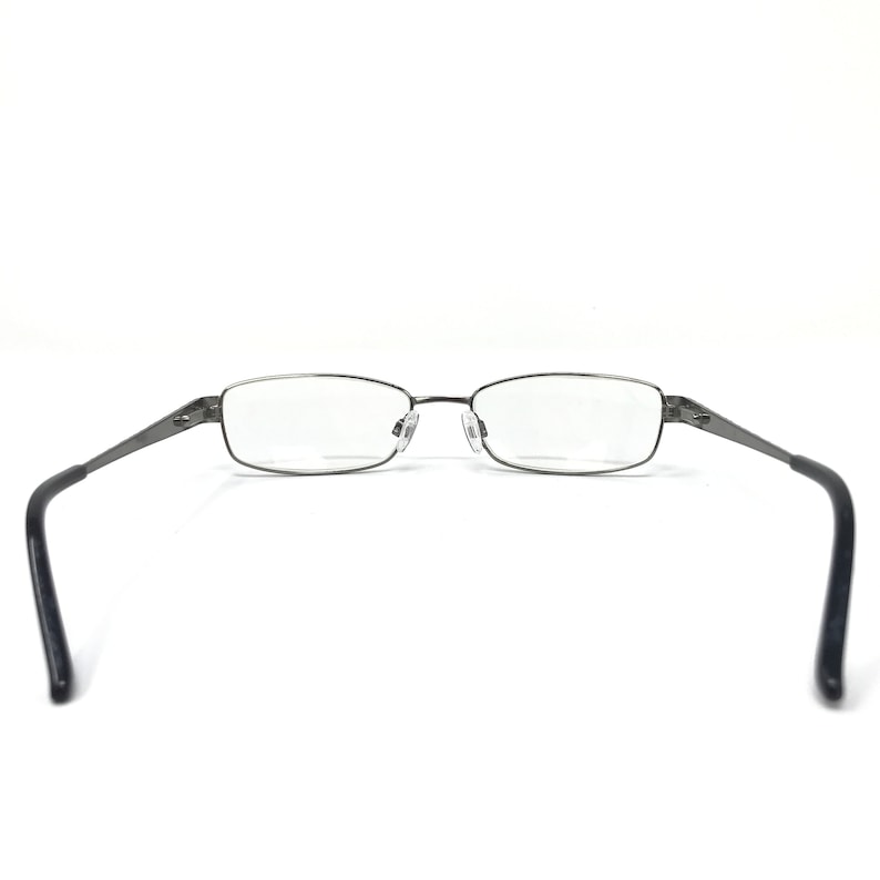 May include: Rectangular eyeglasses with a silver metal frame and dark gray temples. The lenses are clear, and the glasses are set against a white background. The glasses are designed for vision correction.