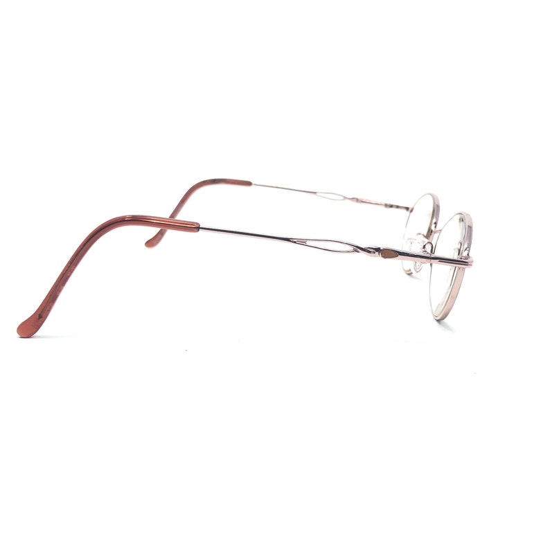 K&ouml;nnte beinhalten: Eine Brille mit einem d&uuml;nnen, silbernen Rahmen und runden Gl&auml;sern. Die B&uuml;gel sind dunkelbraun. Die Brille ist vor einem wei&szlig;en Hintergrund platziert.