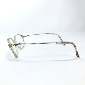 May include: Clear plastic framed glasses with a gold metal bridge and arms. The arms are bent at a 90 degree angle.