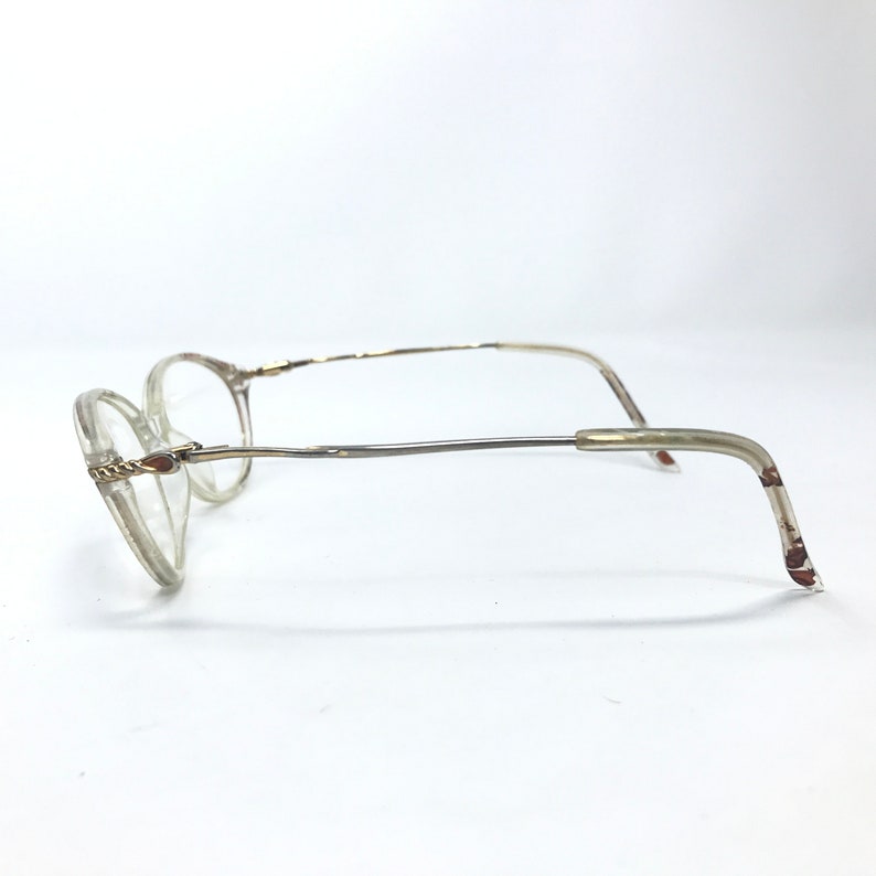 May include: Clear plastic framed glasses with a gold metal bridge and arms. The arms are bent at a 90 degree angle.