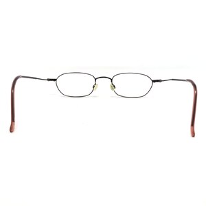 Puede incluir: Gafas ovaladas negras con montura met&aacute;lica fina y patillas marrones. Las lentes transparentes destacan sobre un fondo blanco. Dise&ntilde;o minimalista y cl&aacute;sico.