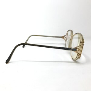 Puede incluir: Un par de gafas doradas con monturas y lentes de pl&aacute;stico transparente. Las monturas tienen un dise&ntilde;o geom&eacute;trico &uacute;nico con un elemento decorativo en el lateral.