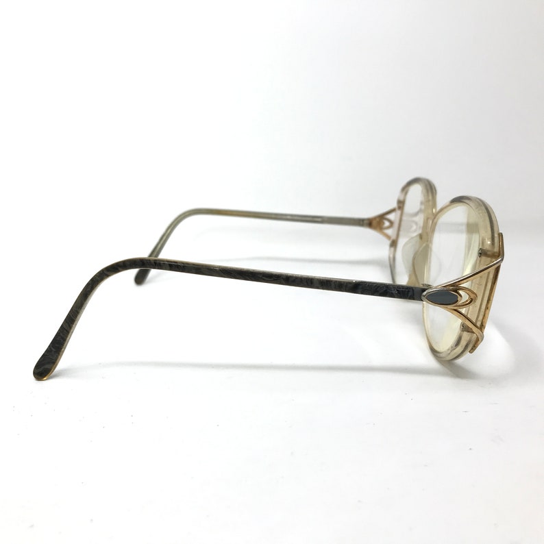 Puede incluir: Un par de gafas doradas con monturas y lentes de pl&aacute;stico transparente. Las monturas tienen un dise&ntilde;o geom&eacute;trico &uacute;nico con un elemento decorativo en el lateral.