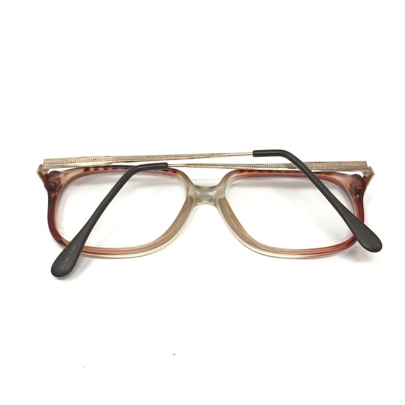 K&ouml;nnte beinhalten: Eine Brille aus braunem und klarem Kunststoff mit einem silbernen Metallrahmen. Die B&uuml;gel der Brille sind schwarz.