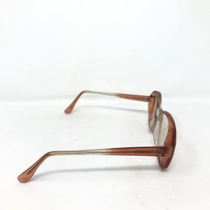 May include: A pair of vintage eyeglasses with a light brown frame and clear lenses. The temples transition from a light color to a darker brown near the ear. The glasses are set against a white background.