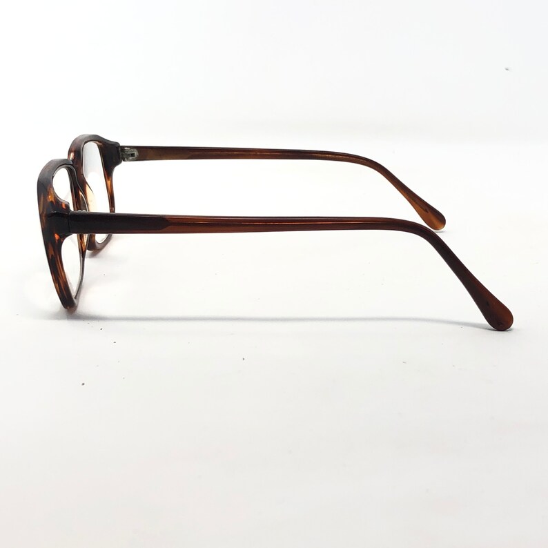 May include: A pair of eyeglasses with a tortoiseshell pattern on the frames. The frames are a mix of brown and amber hues. The temples are a solid brown color, and the lenses are clear.