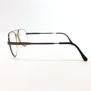 May include: A pair of eyeglasses with a dark brown metal frame and clear lenses. The glasses have a double bridge design and black temple arms. The lenses are rectangular and the overall style is classic.