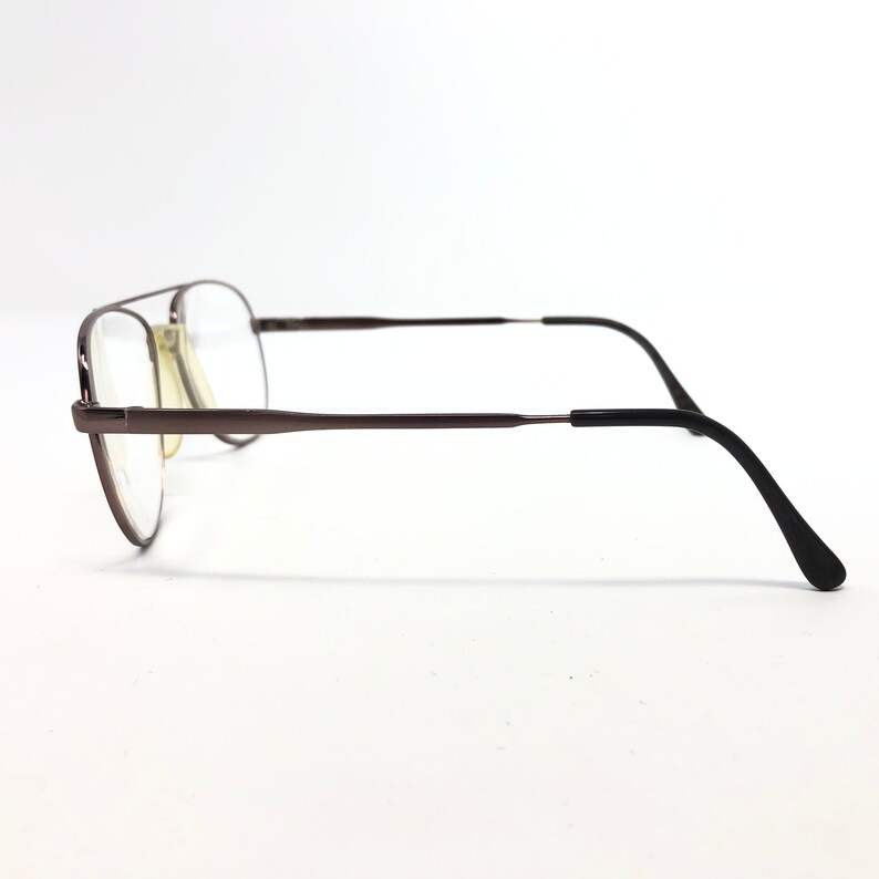 May include: A pair of eyeglasses with a dark brown metal frame and clear lenses. The glasses have a double bridge design and black temple arms. The lenses are rectangular and the overall style is classic.