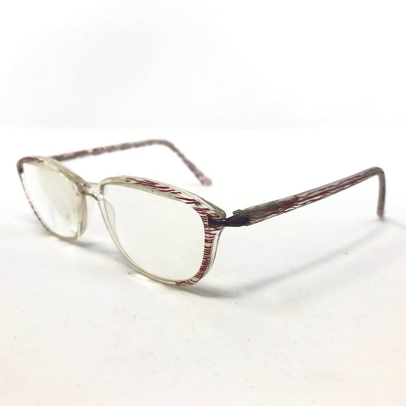 May include: Clear eyeglasses with a rectangular frame and a red striped pattern on the edges and arms. The lenses are clear, and the frame is a light, translucent color. The arms have a curved design.