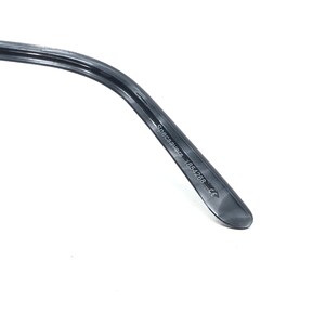 May include: Close-up of a dark grey glasses arm. The text "Specsavers 1854268 CE" is printed on the arm. The arm curves and narrows to a rounded end. The background is white.