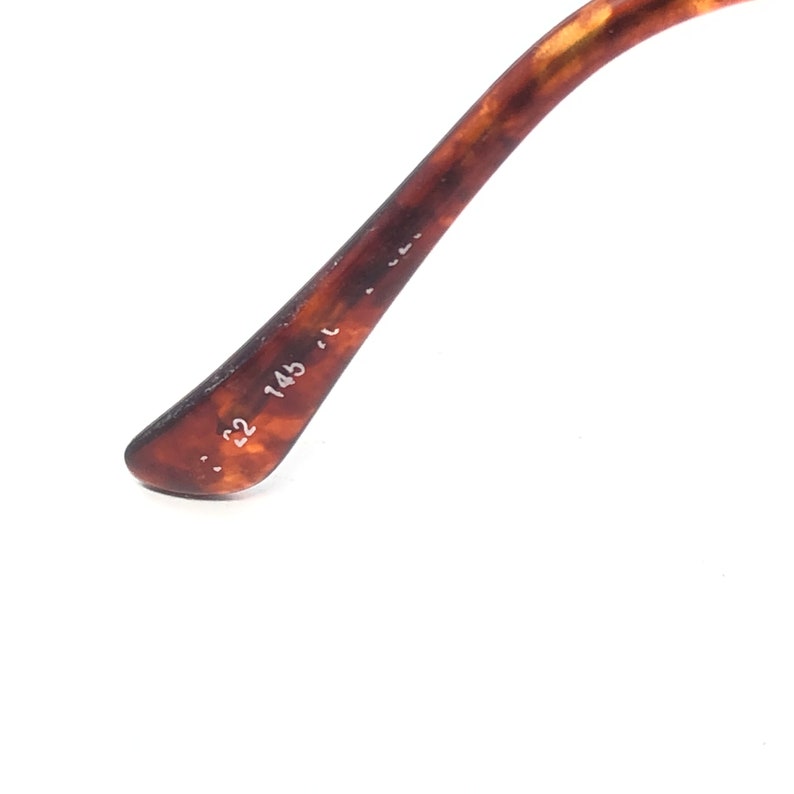 May include: Close-up of the arm of a pair of eyeglasses. The arm is a tortoiseshell pattern with brown and amber tones. The numbers "52 145" are printed on the arm.