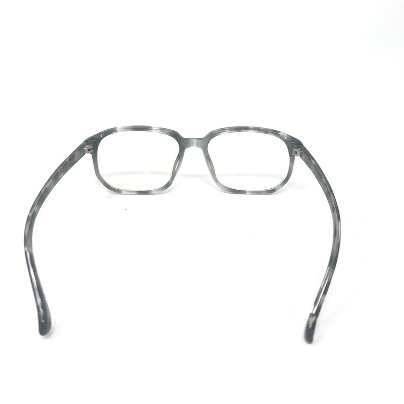 Puede incluir: Gafas con montura rectangular con estampado gris y blanco. Las gafas tienen un dise&ntilde;o cl&aacute;sico con un patr&oacute;n sutil en la montura y las patillas. Las lentes son transparentes y las patillas se curvan suavemente.