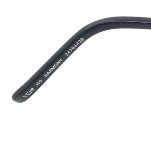 May include: Close-up of a black eyeglass arm. The arm has the text "HARMONY 24764438" printed on it. The arm also has the measurements "5 18 140" printed on it.