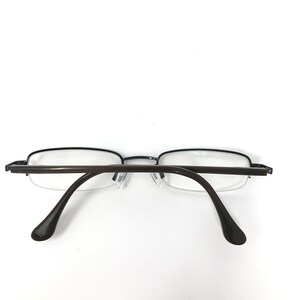K&ouml;nnte beinhalten: Eine Brille mit einem dunkelbraunen Rahmen und B&uuml;geln. Die Gl&auml;ser sind klar, und der Rahmen hat eine rechteckige Form. Die Brille ist vor einem wei&szlig;en Hintergrund platziert.