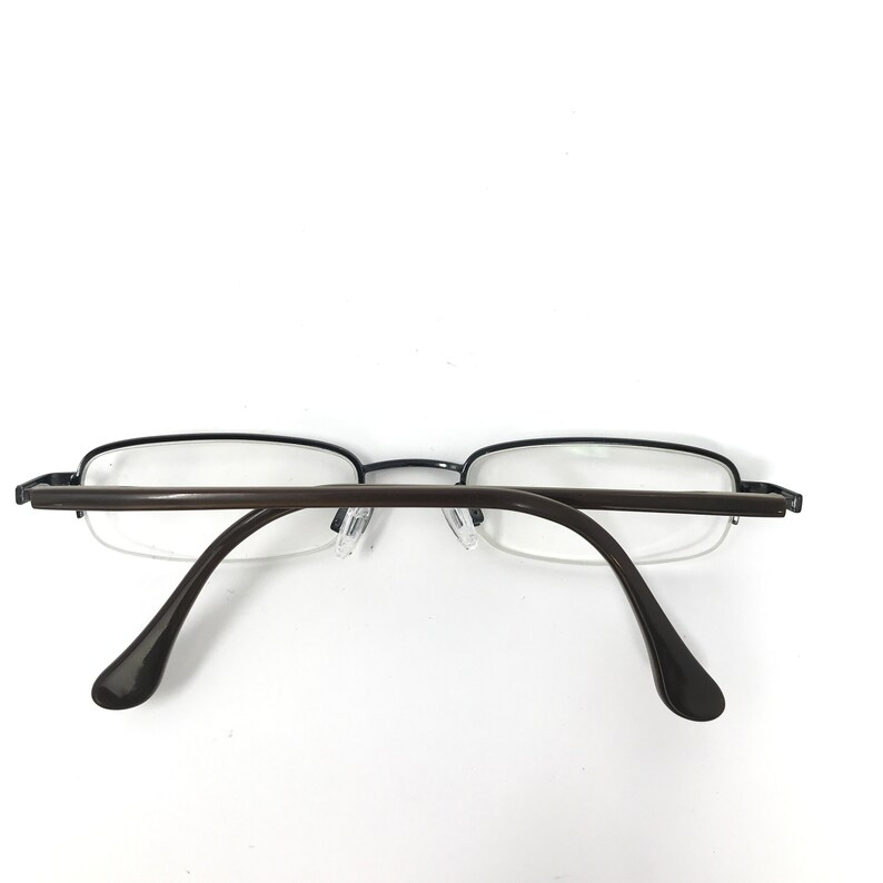 K&ouml;nnte beinhalten: Eine Brille mit einem dunkelbraunen Rahmen und B&uuml;geln. Die Gl&auml;ser sind klar, und der Rahmen hat eine rechteckige Form. Die Brille ist vor einem wei&szlig;en Hintergrund platziert.
