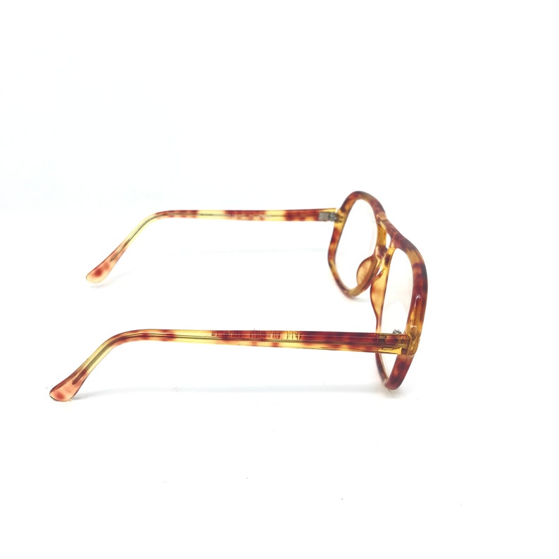May include: A pair of eyeglasses with a tortoiseshell pattern. The frames are a mix of brown and yellow, with a geometric shape. The temples are thin and extend to the ear pieces. The lenses are clear.