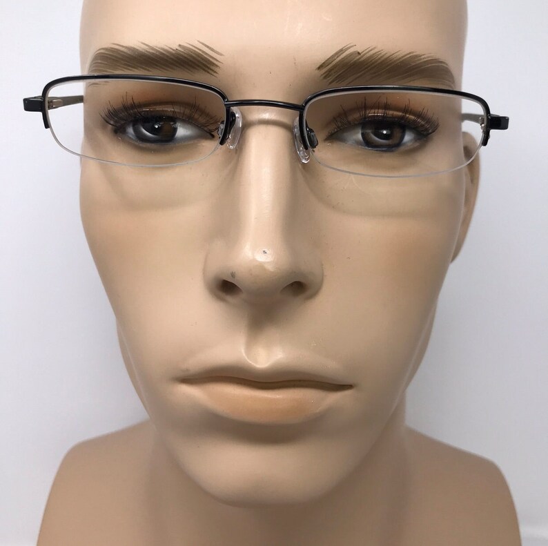 K&ouml;nnte beinhalten: Schwarze Halbrandbrille mit rechteckigem Rahmen und klaren Gl&auml;sern. Die Brille wird auf einem Schaufensterkopf pr&auml;sentiert. Der Rahmen hat ein schlankes, elegantes Design und die Gl&auml;ser haben eine klassische Form.