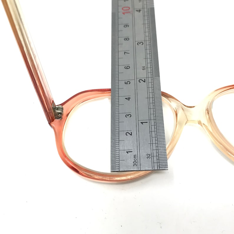 May include: A pair of pink and clear plastic glasses with a ruler measuring the width of the glasses at 4.5 cm.