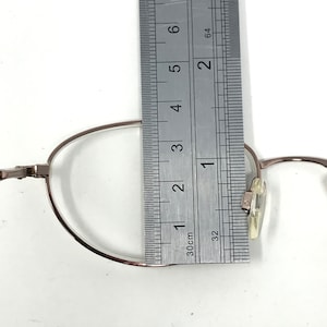 Op de afbeelding: Zilverkleurige metalen bril met een flexibel montuur. Het montuur wordt gemeten met een liniaal, wat een meting van 3,5 cm laat zien.