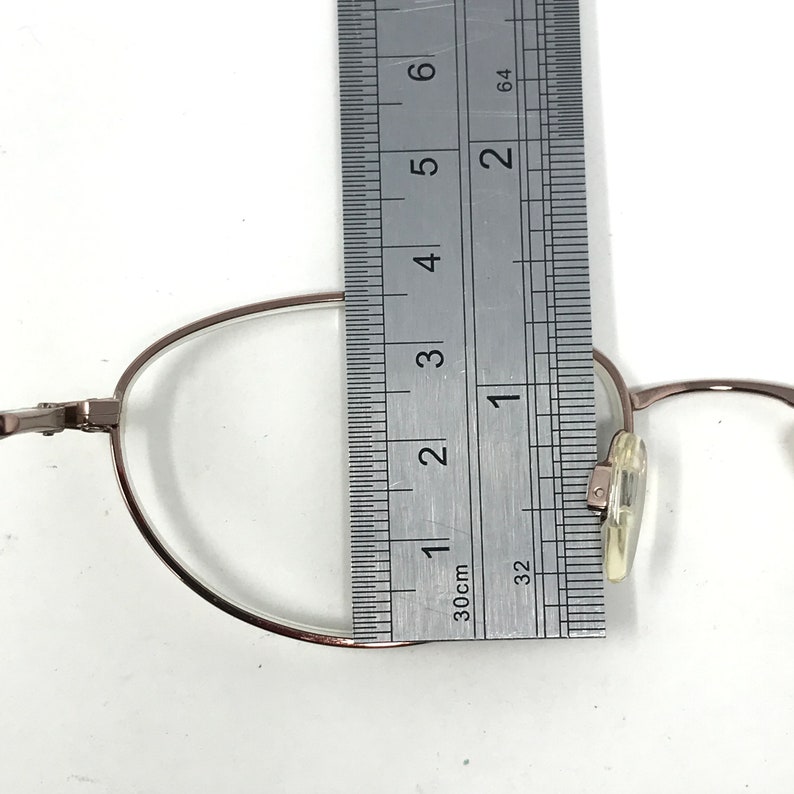 Op de afbeelding: Zilverkleurige metalen bril met een flexibel montuur. Het montuur wordt gemeten met een liniaal, wat een meting van 3,5 cm laat zien.