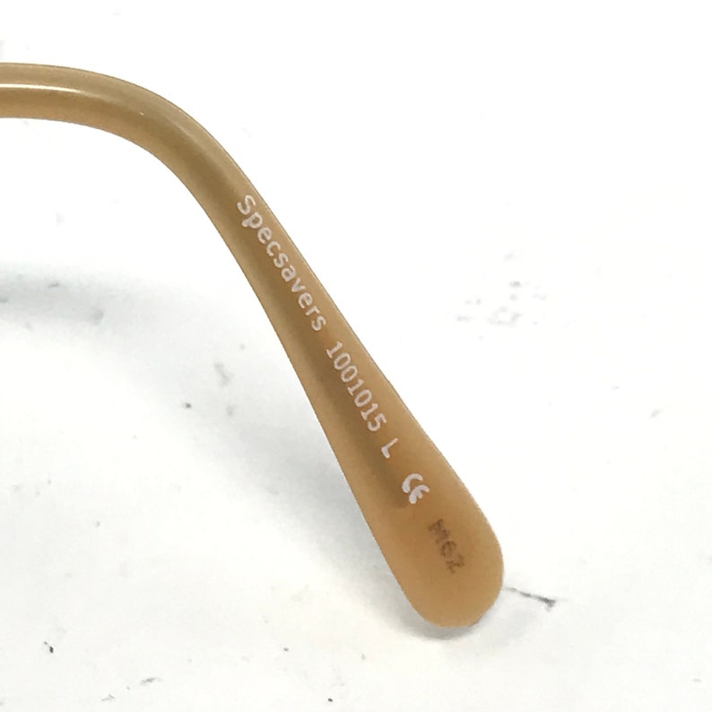 Peut inclure: Gros plan sur la branche marron d'une paire de lunettes avec le texte "Specsavers 1001015 L CE M62" imprim&eacute; sur la branche.