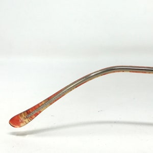 May include: Close-up of the arm of a pair of eyeglasses. The arm is a mix of orange, red, and yellow patterns. The text "46-16-135 TOWN & COUNTRY" is printed on the arm.