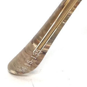 May include: Close-up of the inside of a brown and gold-toned eyeglass frame with the text "54 15-135" engraved on the inside.