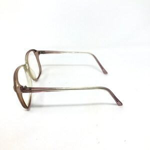 May include: A pair of eyeglasses with a light brown frame and clear lenses. The temples are a gradient, transitioning from light brown to clear. The glasses are set against a white background.